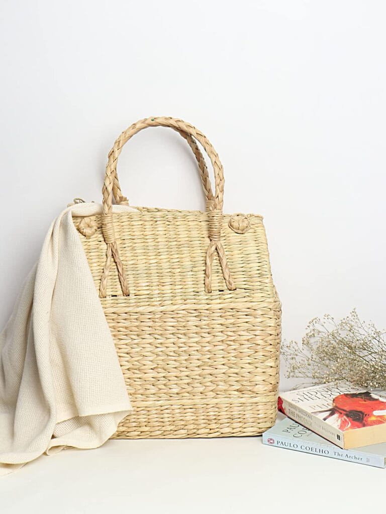 A minimalist handwoven wicker picnic basket resting on a neutral blanket, perfect for a slow weekend outdoors.